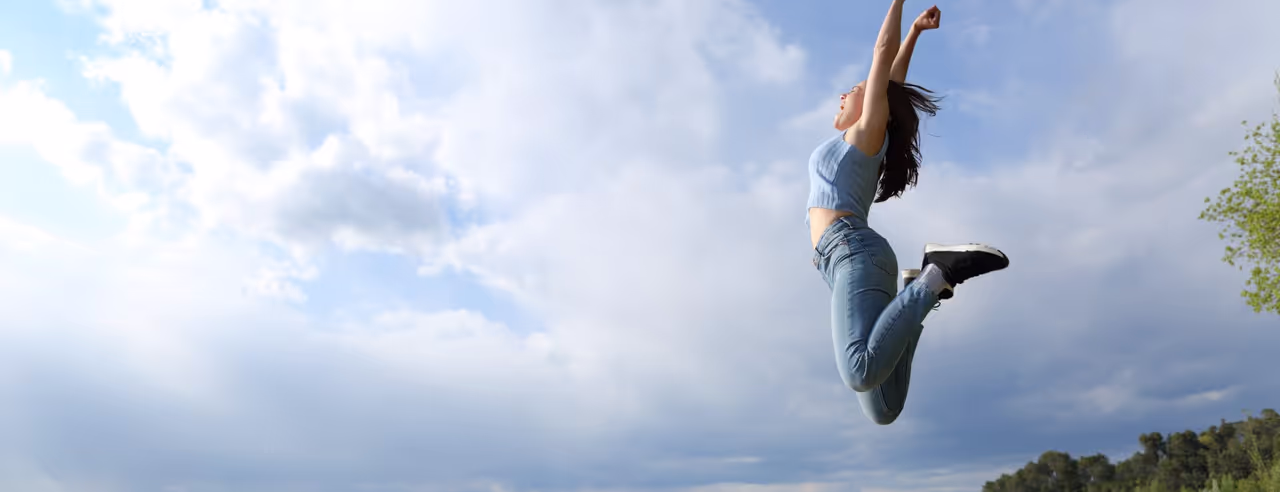 Frau springt voller Energie in die Luft vor blauem Himmel