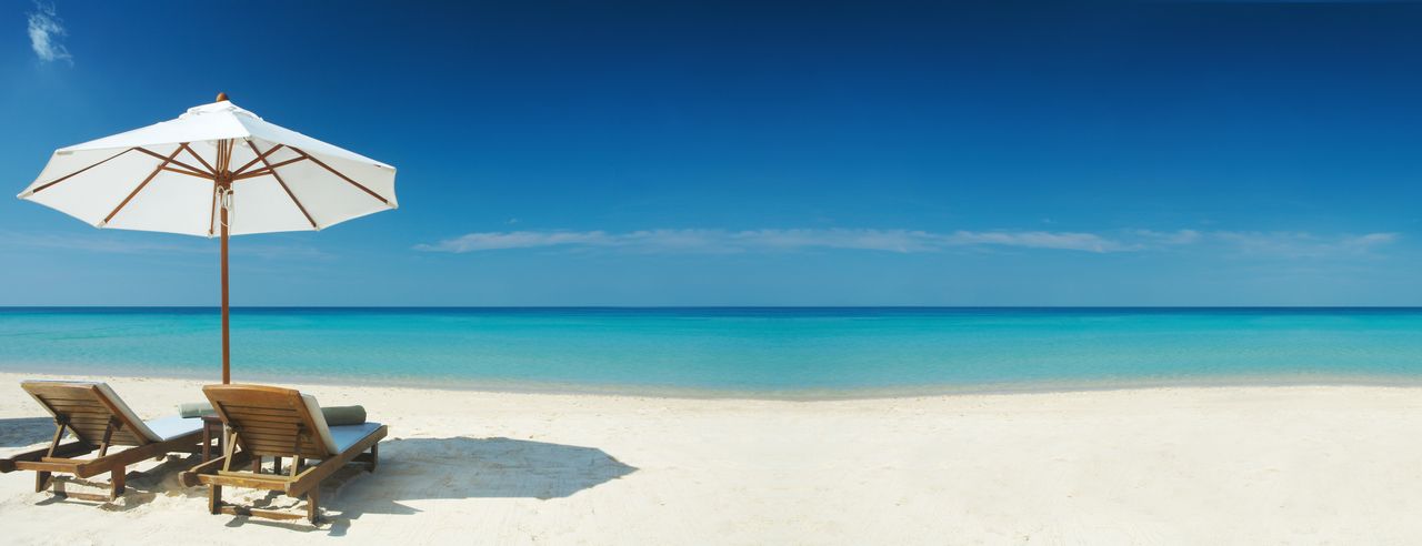 Weißer Strand und blaues Meer, Sonnenschirm und Liegen bei einem Langzeiturlaub
