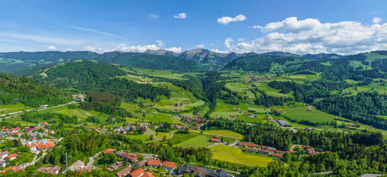Blick auf die roten Dächer Oberstaufens zwischen grünen Feldern und Wäldern