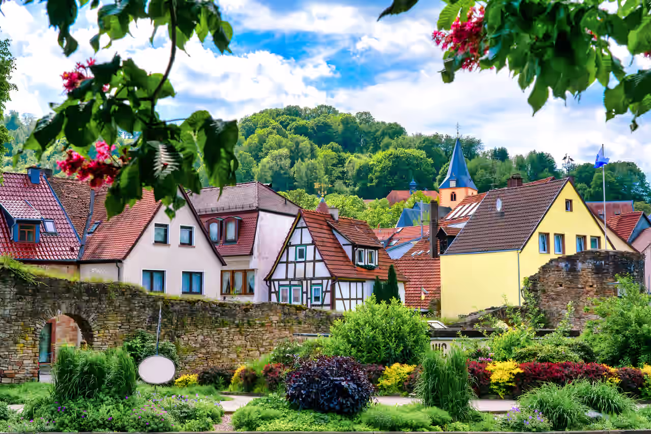 Gartenanlage unterhalb der Stadtmauer von Bad Orb mit Fachwerkhäusern und farbenfrohen Anstrichen vor einem leuchtend grün bewaldeten Hügel