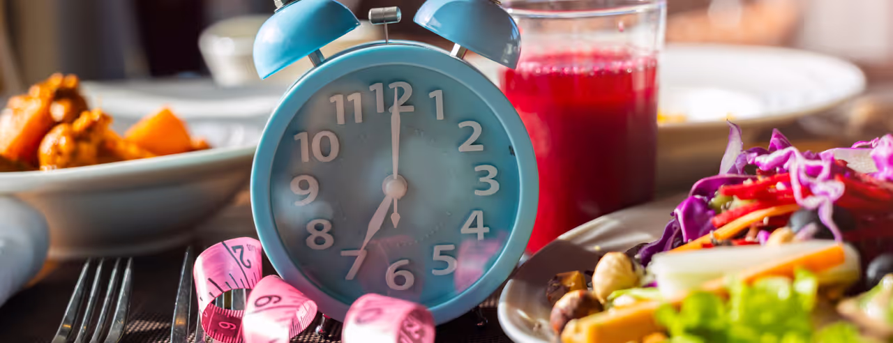 Blauer Wecker und rosafarbenes Maßband neben einem Teller mit Salat und einem Glas mit rotem Saft