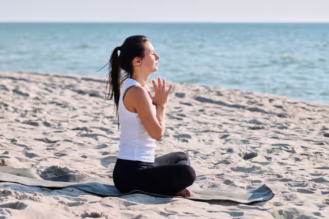 Frau macht Yoga auf einer Matte auf dem Sandstrand an der Ostsee