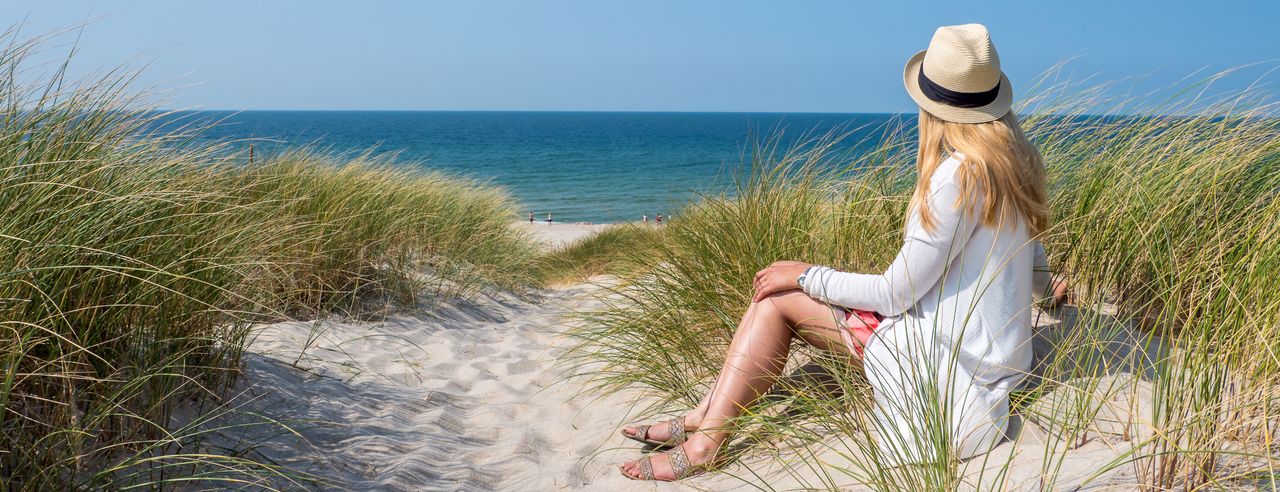 Frau mit Hut sitzt an einem am Strand an der Nordsee