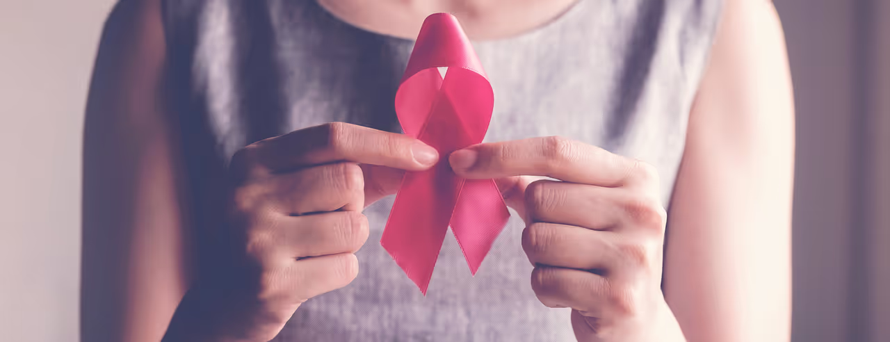 A woman holds the pink ribbon in front of her