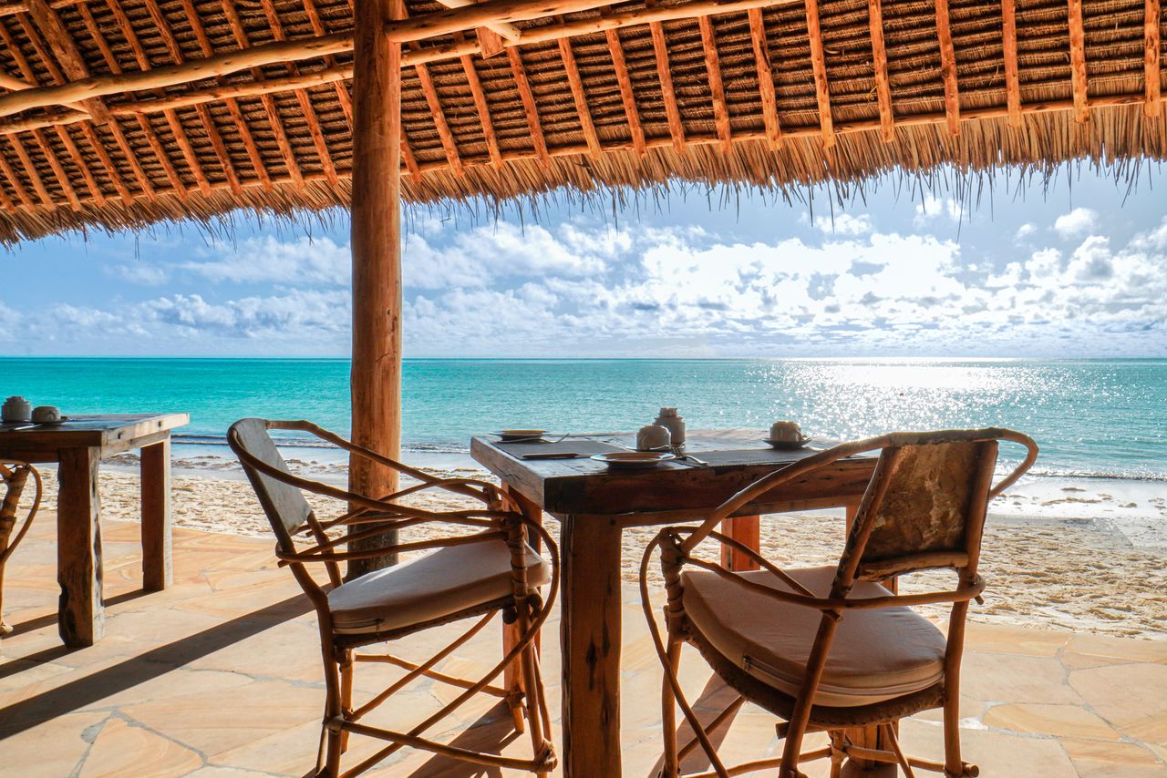 Tisch und zwei Stühle in einem Strandrestaurant mit Sandstrand und blauem Meer im Hintergrund