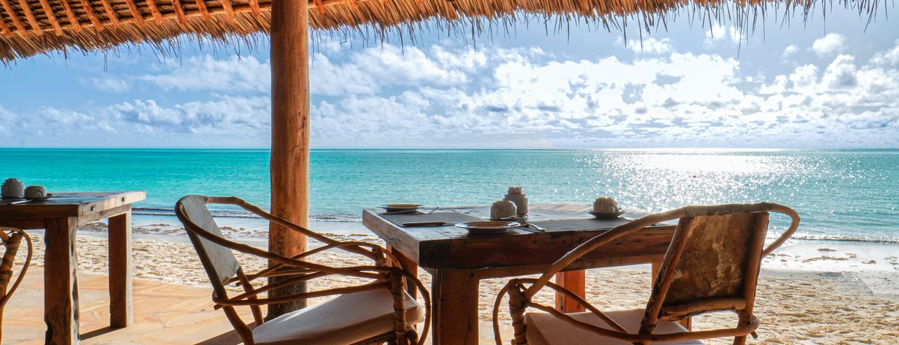 Tisch und zwei Stühle in einem Strandrestaurant mit Sandstrand und blauem Meer im Hintergrund