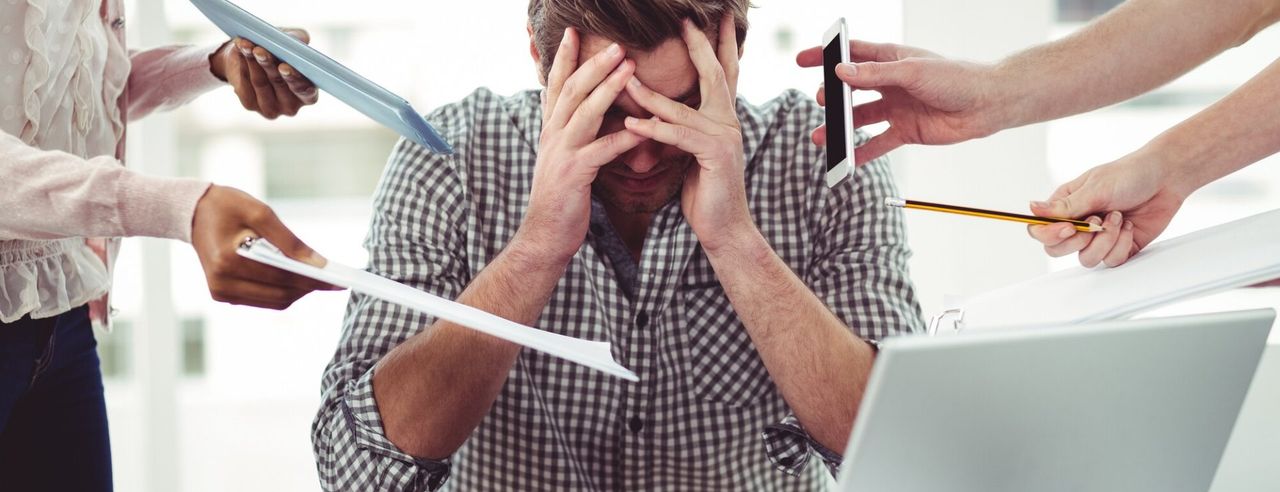 Mann hält sich den Kopf währen ihm Handys, Papiere und Stifte hingehalten werden