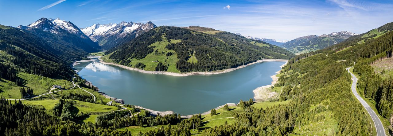 Der Durlassboden Speicher zwischen bewaldeten Berghängen, im Hintergrund die Alpen.