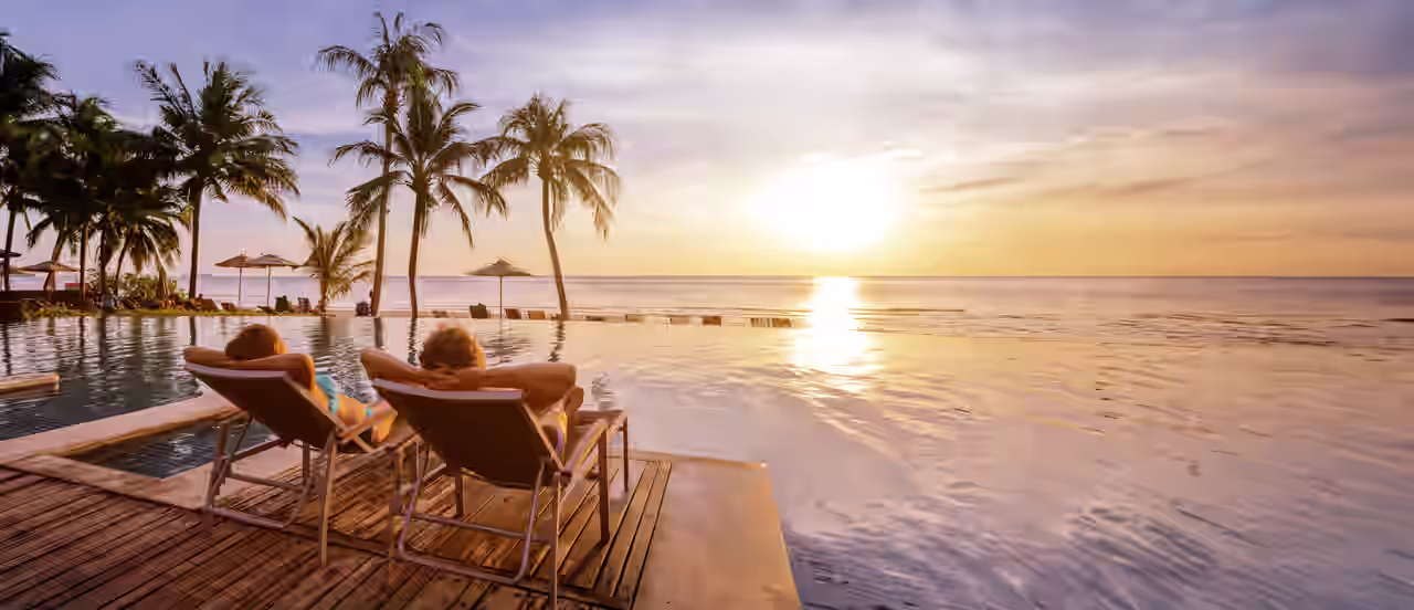 Ein Paar auf zwei Liegen mit Blick auf einen Pool und das Meer