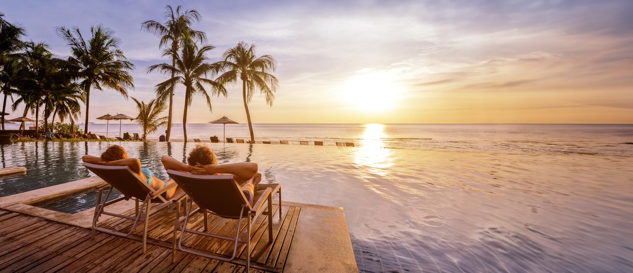 Ein Paar auf zwei Liegen mit Blick auf einen Pool und das Meer