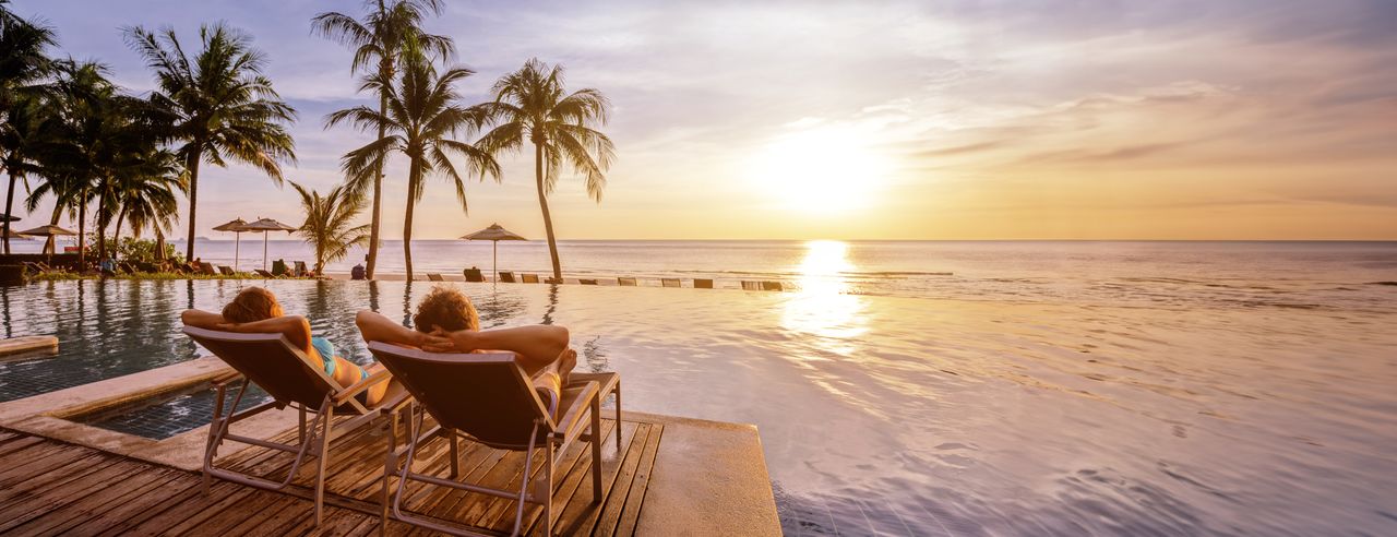 Ein Paar auf zwei Liegen mit Blick auf einen Pool und das Meer