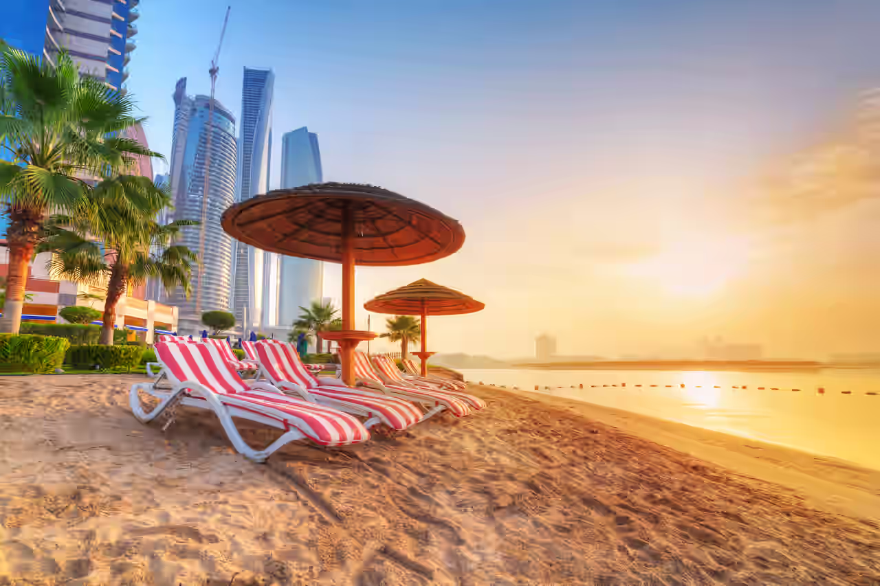 Strand mit Palmen, roten Liegestühlen und Skyline in Dubai