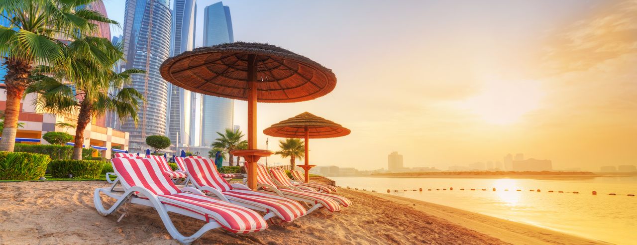 Strand mit Palmen, roten Liegestühlen und Skyline in Dubai