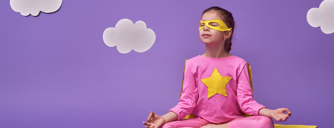 EIn Kind im Superhelden-Kostüm nimmt den Lotussitz ein