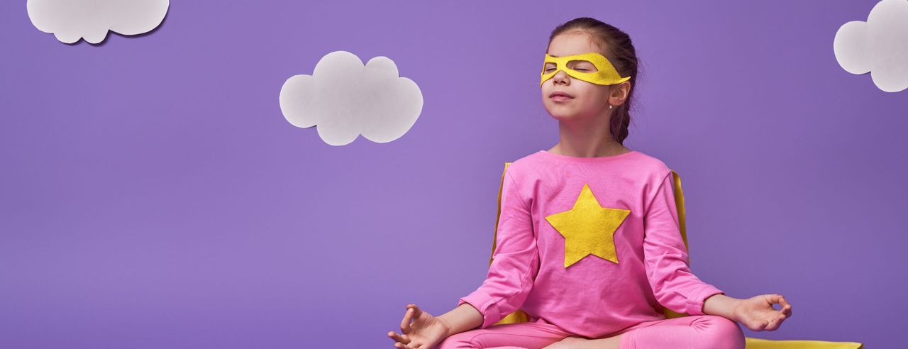 EIn Kind im Superhelden-Kostüm nimmt den Lotussitz ein