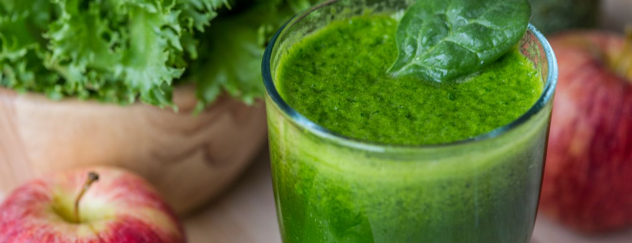 Grüner Saft im Glas mit Äpfeln und grünem Gemüse im Hintergrund