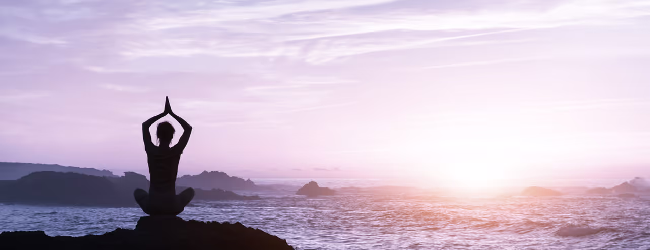Dunkle Silhouette einer Frau, die Yoga am Meer macht.