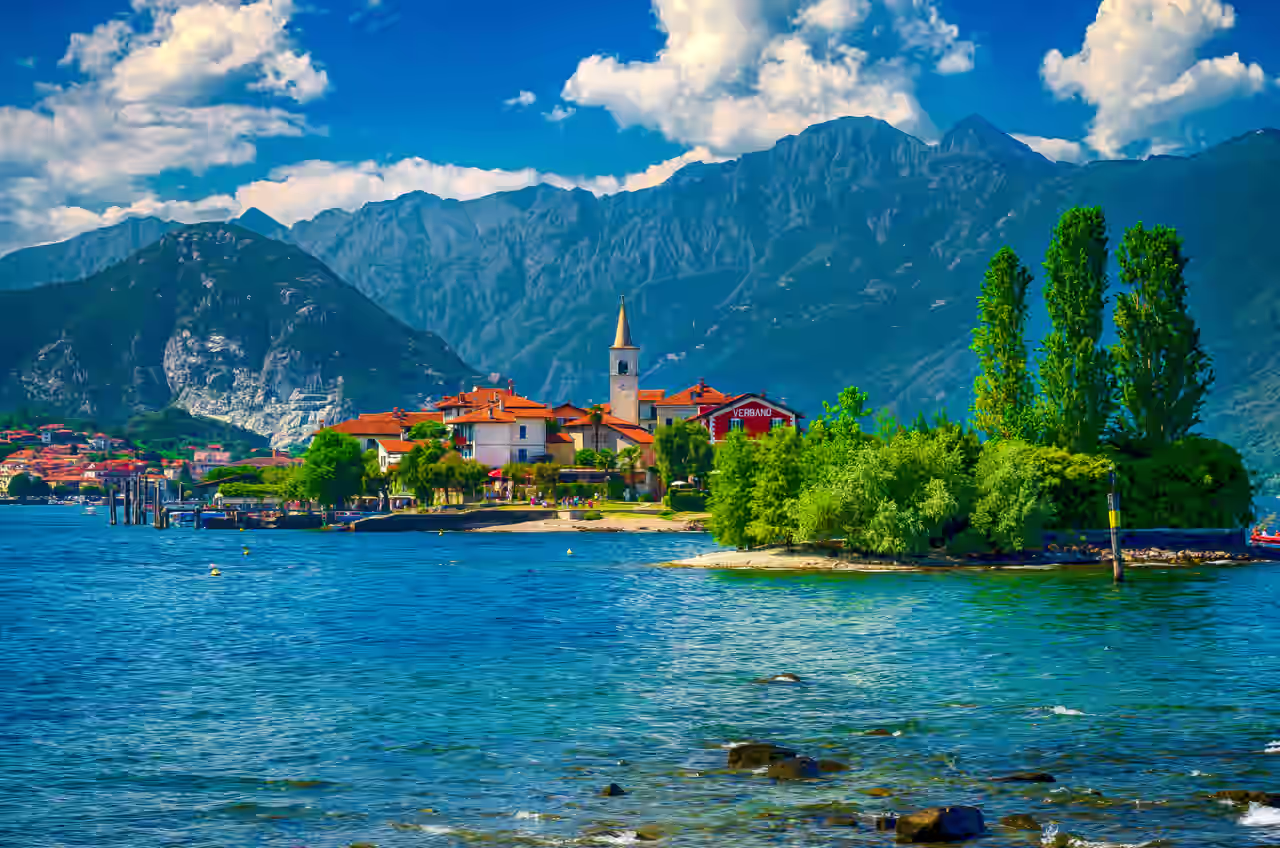 See mit kleinem Ort im Hintergrund und Gipfeln