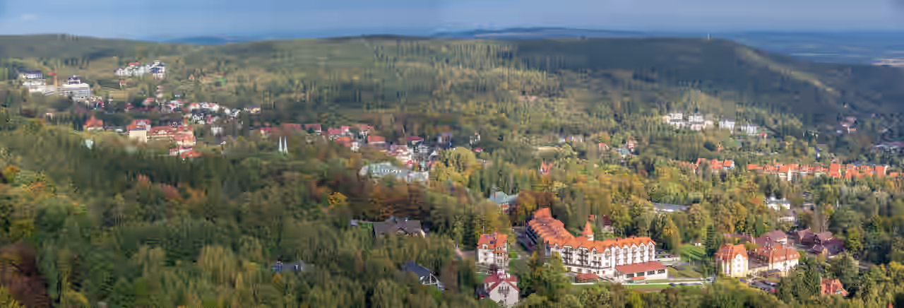 Häuser von Bad Flinsberg mit roten, schwarzen und grünen Dächern zwischen Bäumen und bewaldeten Hügeln