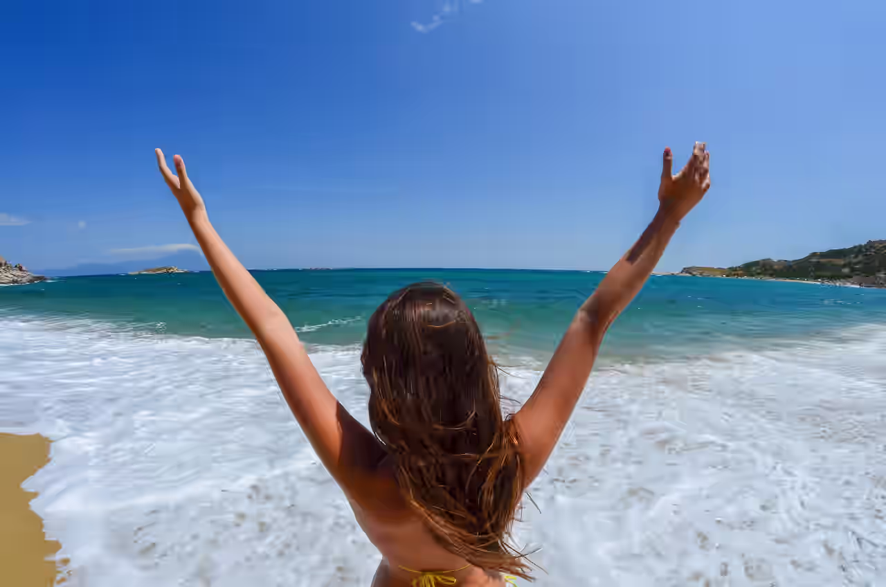 Eine Frau streckt die Arme in die Höhe am Meer und schaut auf das Wasser während ihrer Yogalehrer Ausbildung