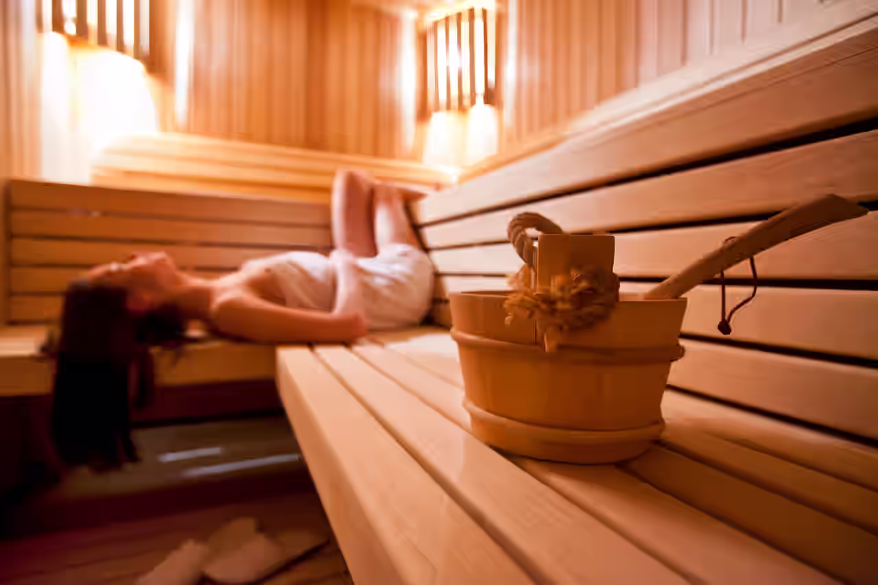 Eine Frau liegt auf dem Rücken in der Sauna und genießt Ihren Urlaub mit Sauna in NRW. Im Vordergrund steht ein Holzeimer auf der hölzernen Saunabank.