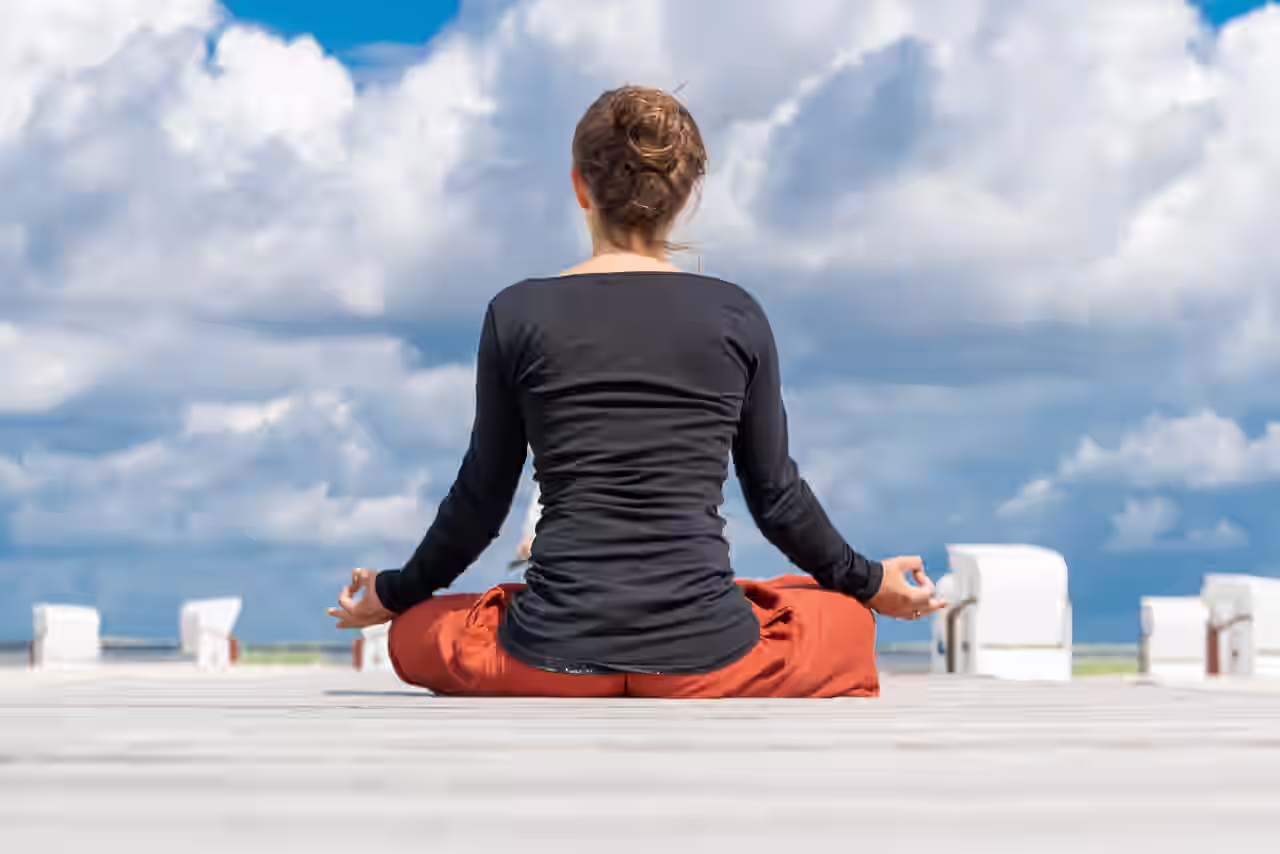 Eine Frau praktiziert Yoga auf Rügen mit dem Blick aufs Meer auf einem Steg.