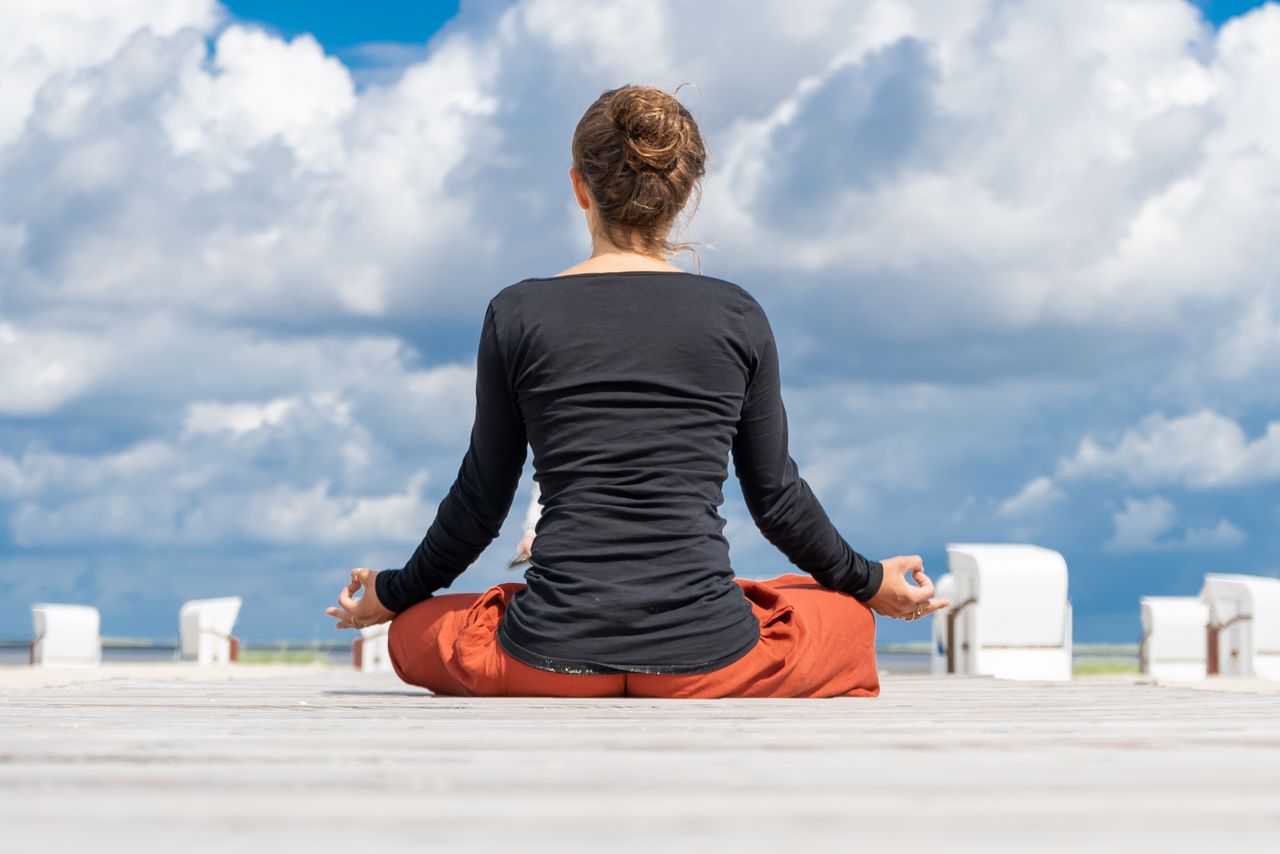 Eine Frau praktiziert Yoga auf Rügen mit dem Blick aufs Meer auf einem Steg.