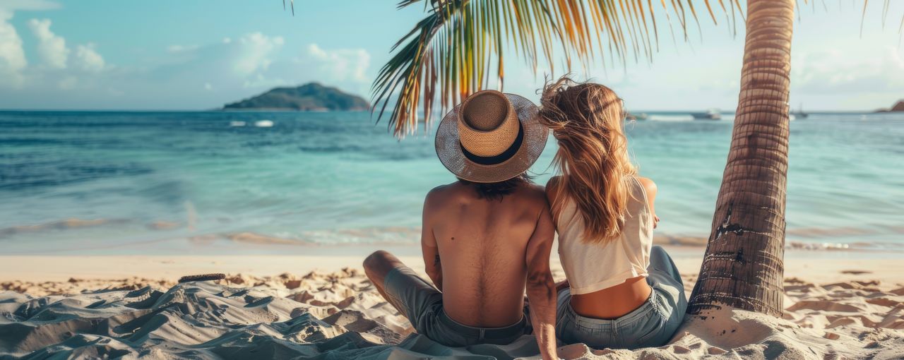 Ein Paar sitzt unter einer Palme am Strand in ihren Flitterwochen
