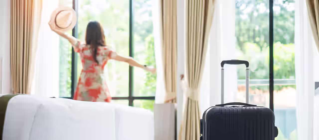 Eine Frau schaut aus dem Fenster Ihres Hotelzimmers und streckt die Arme von sich