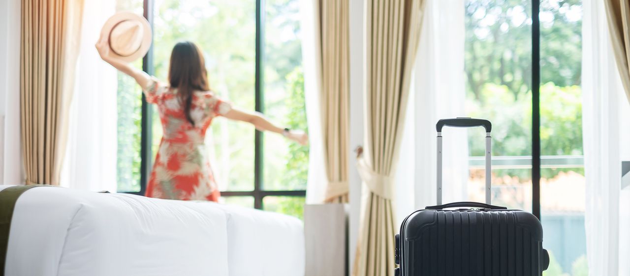 Eine Frau schaut aus dem Fenster Ihres Hotelzimmers und streckt die Arme von sich