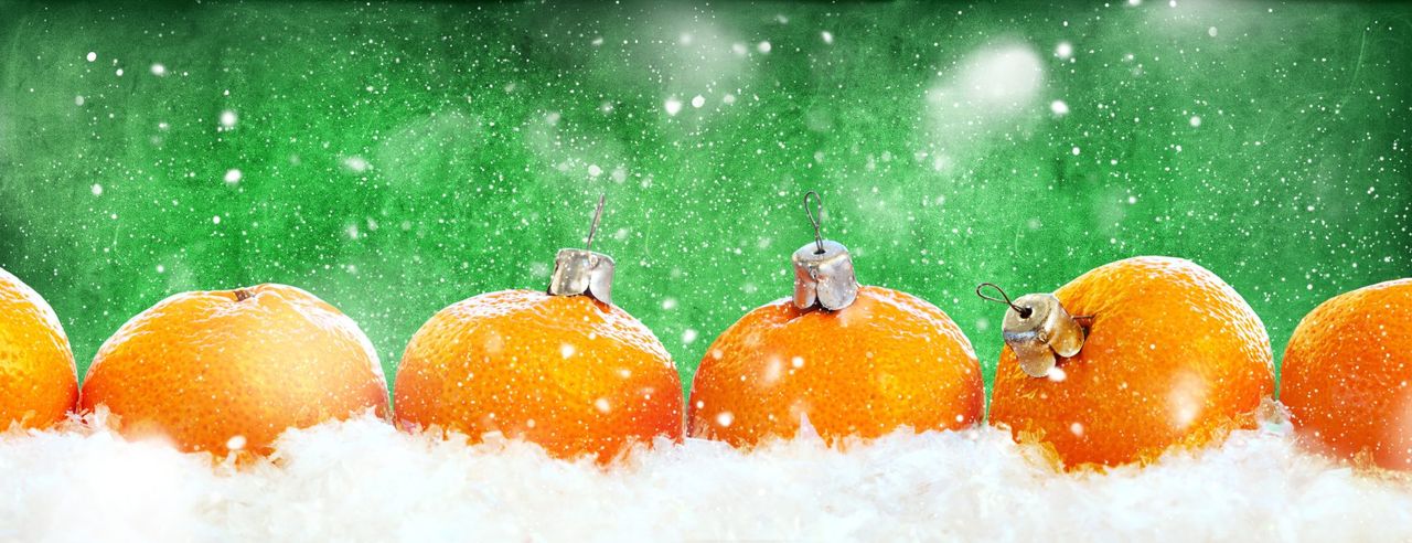 Eine Mischung aus Orangen und Christbaumkugeln vor winterlichem Hintergrund
