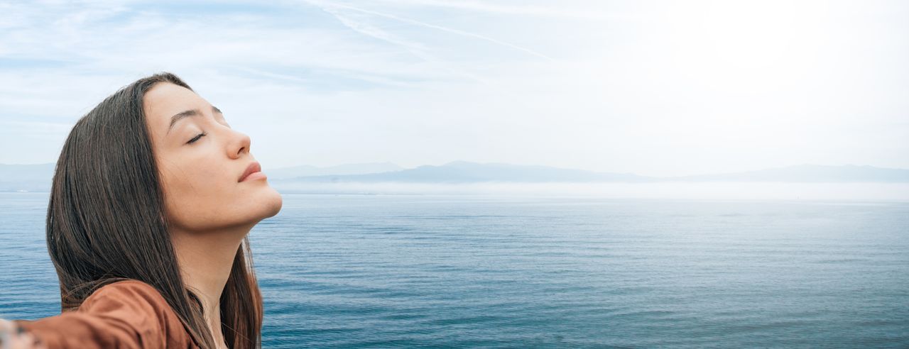 Ein Mädchen atmet entspannt im Freien mit dem Meer im Hintergrund