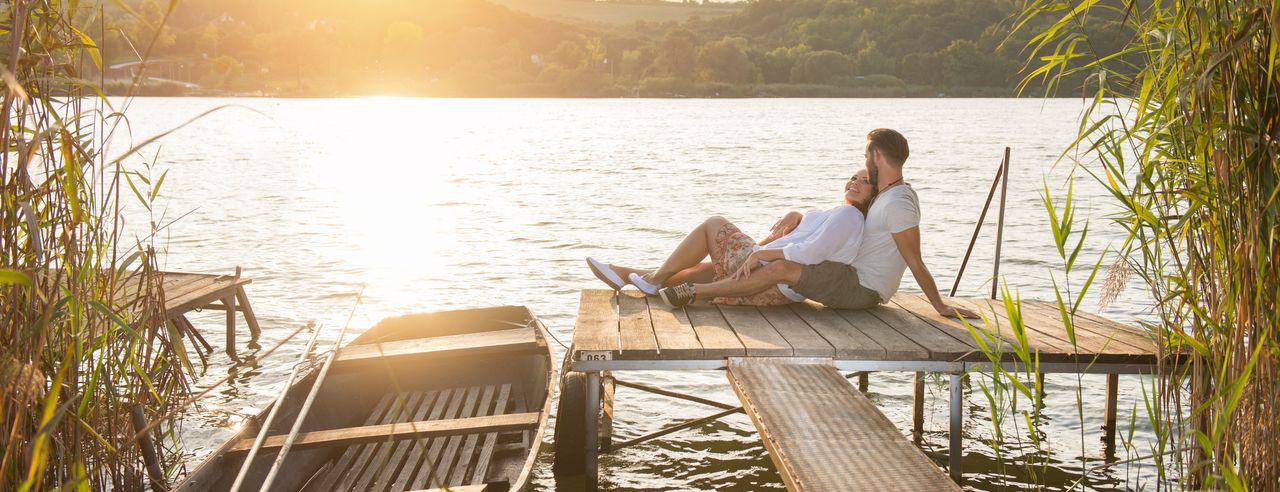 Paar sitzt im warmen Sonnenlicht auf einem Steg am See