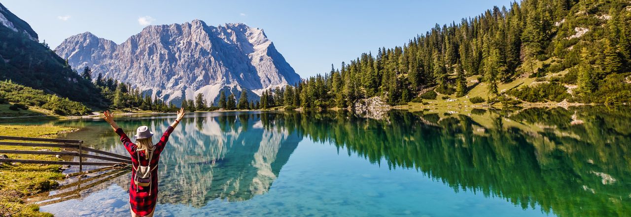 Eine Frau an einem Bergsee streckt die Arme in die Luft