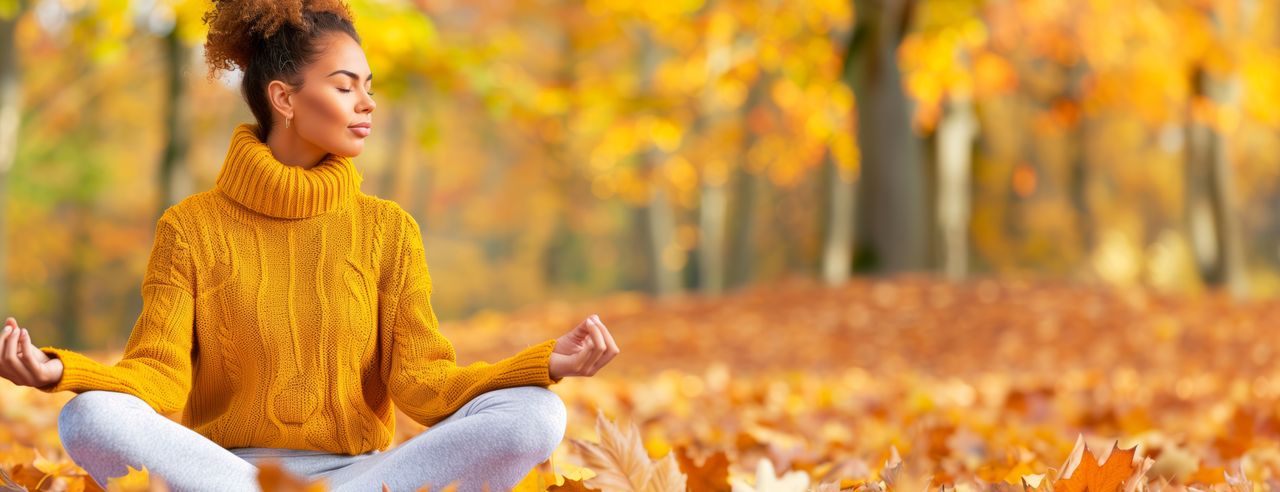 Eine Frau sitzt in einem Wald im Herbst und übt Yoga um ihr Immunsystem zu stärken