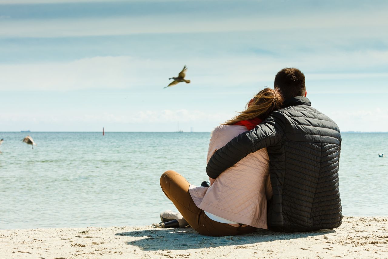 Ein Paar sitzt Arm in Arm am Strand beim Romantikurlaub in Schleswig-Holstein