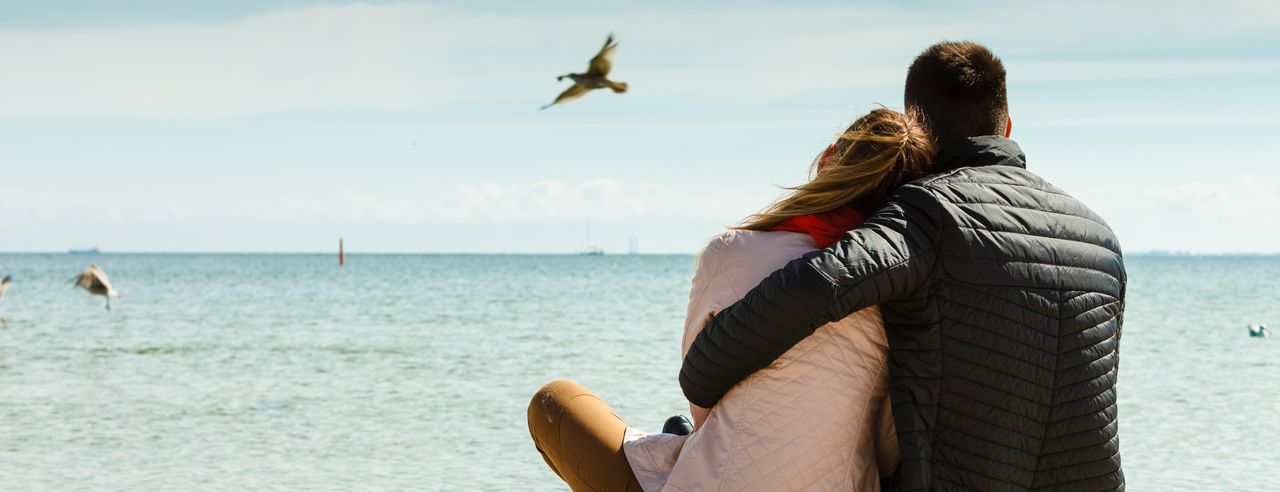 Ein Paar sitzt Arm in Arm am Strand beim Romantikurlaub in Schleswig-Holstein