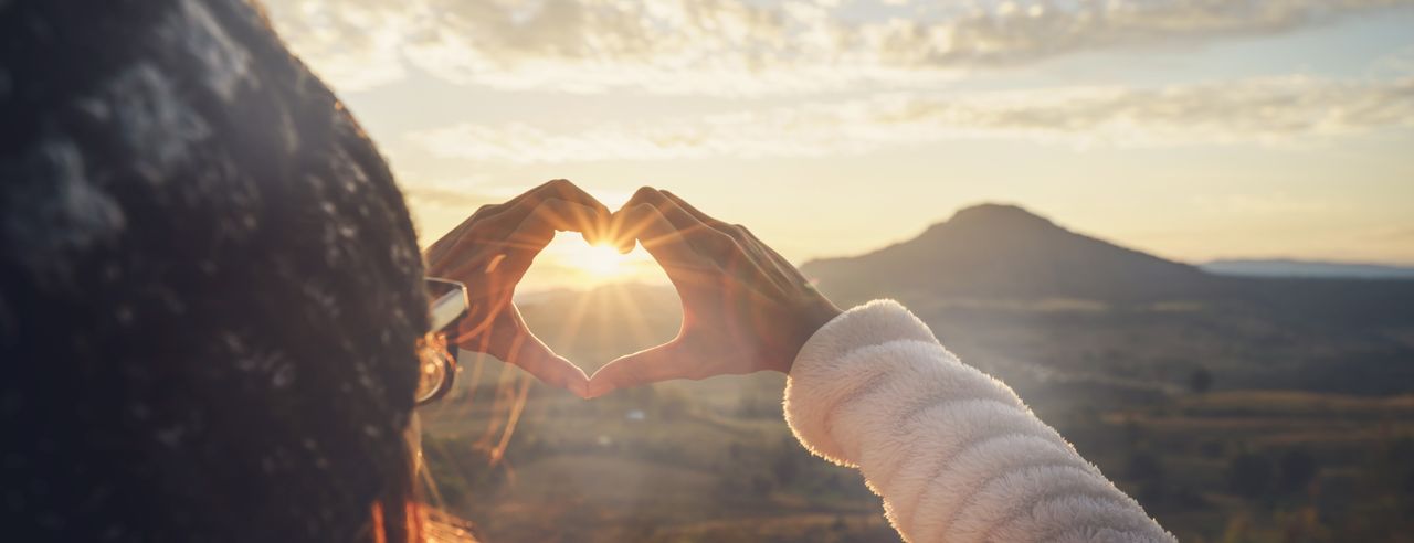 Frau formt Herz mit Ihren Händen vor einem Bergpanorama eines romantischen Hotels in Bayern