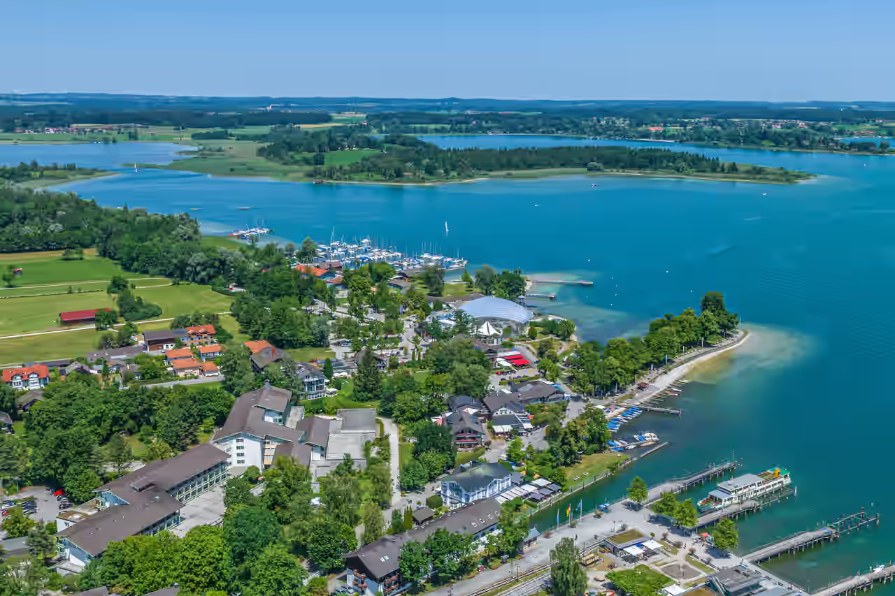 Blick auf Prien am Chiemsee umgeben von grünen Wiesen und Bäumen sowie dem blauen Wasser des Sees