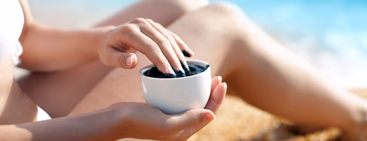 A woman holds a bowl of fango mud and dips her fingers into it