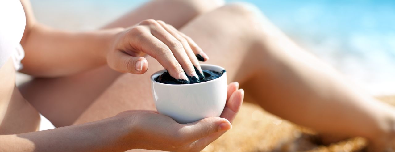 A woman holds a bowl of fango mud and dips her fingers into it