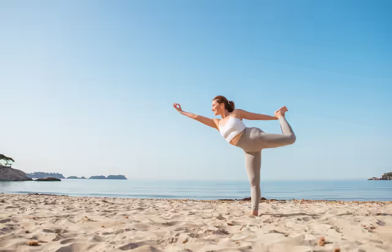 Frau in der Yoga Tänzer Pose am Strand vor ruhigem Meer