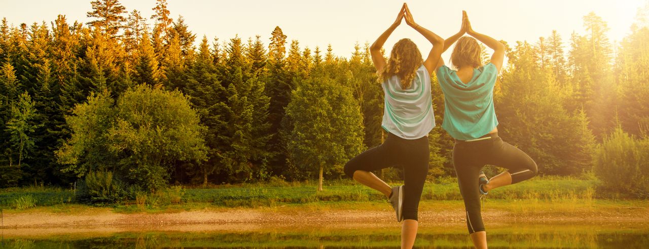 Zwei junge hübsche Frauen praktizieren Yoga auf Holzsteg am See im Herbst im Schwarzwald