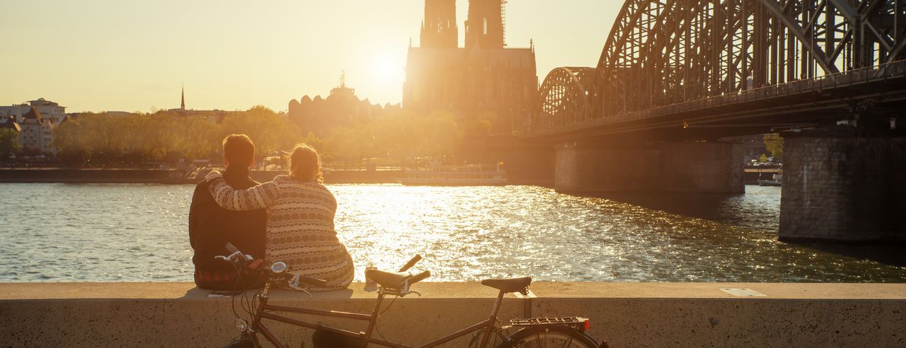 Pärchen sitze bei Sonnenuntergang am Rhein und blick auf den Kölner Dom