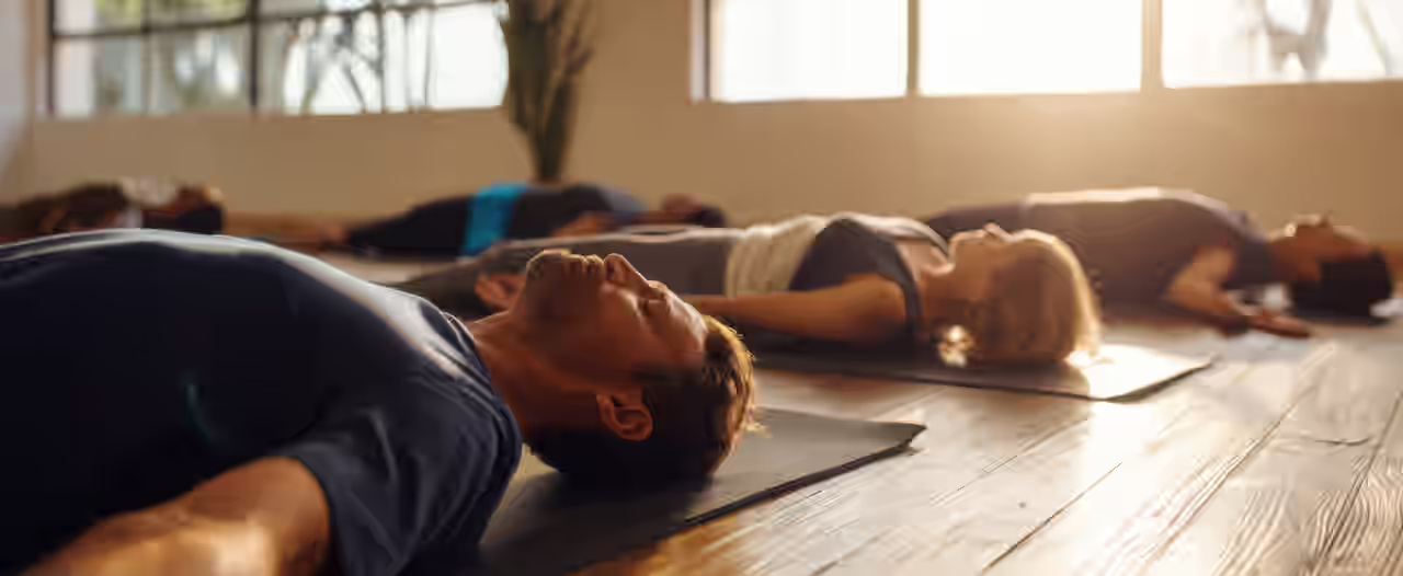 Eine Gruppe in der Yogatherapie liegt auf Yogamatten gebettet am Boden