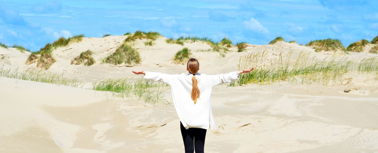 Eine Frau steht in Mecklenburg-Vorpommern am Strand und breitet die Arme aus