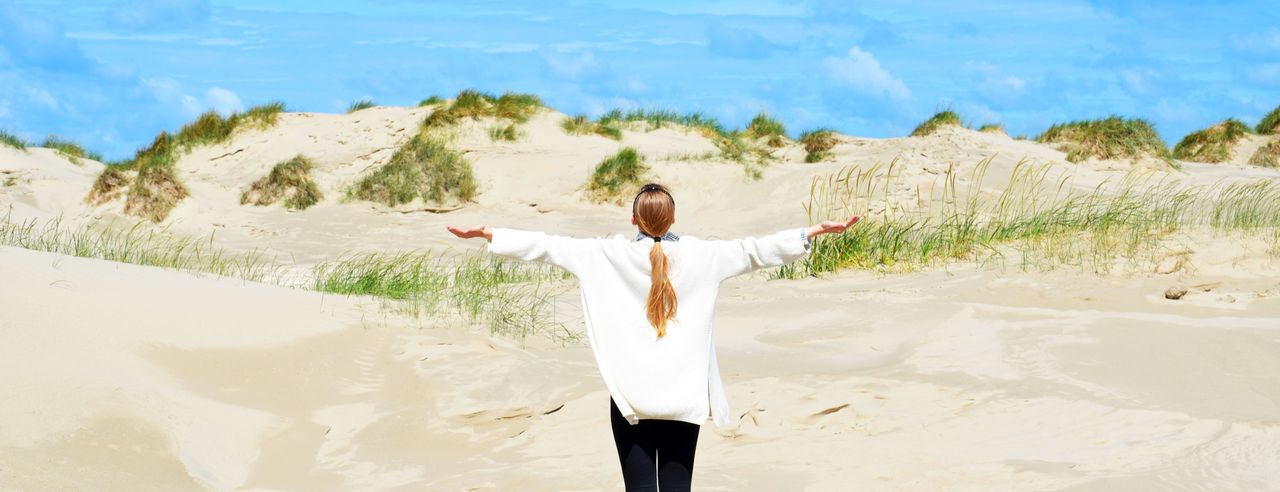Frau steht mit dem Rücken zum Meer und blickt auf die Dünen der Ostsee