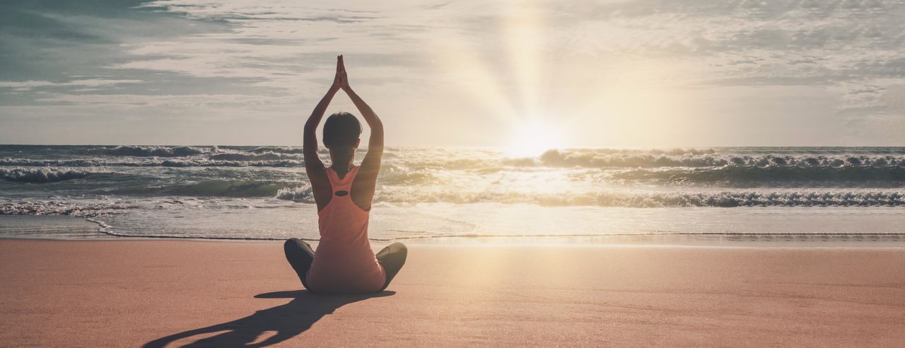 Frau macht Hatha Yoga bei Sonnenaufgang am Strand