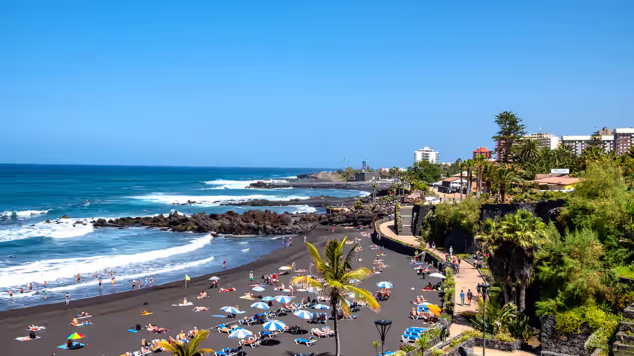 Liegen und Sonnenschirme auf dem schwarzen Sandstrand Playa Jardin an der Nordküste von Teneriffa