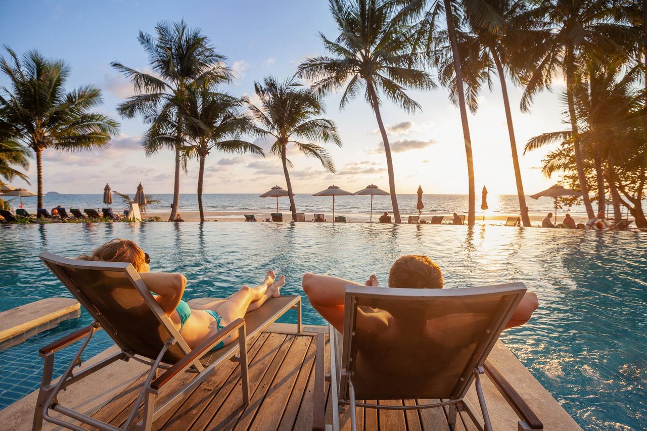 Ein Pärchen entspannt sich auf Liegestühlen am Pool mit Blick auf das Meer und die Palmen.